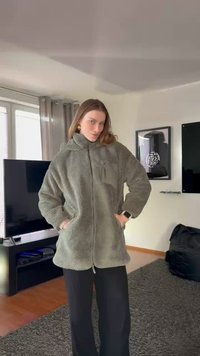 Groene fleecejas met een hoge kraag, ritssluiting aan de voorkant en zijzakken. Gestructureerd oppervlak, ruime pasvorm, gedragen over een zwarte broek.