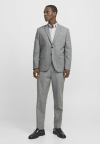 Pilkas kostiumas su pritaikytu siluetu, dviem mygtukais, su įpjovomis atlapais ir suderintomis kelnių. Stiliuotas su dryžuota marškiniais ir juodais batais.