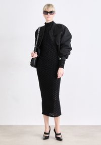 Black knit dress with geometric pattern, paired with a puffy black bomber jacket, and black high-heeled shoes. Accessories include large sunglasses.