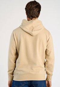 Felpa con cappuccio beige chiaro in tessuto morbido con tasca a marsupio, cappuccio e polsini a costine, cuciture visibili e vestibilità rilassata.