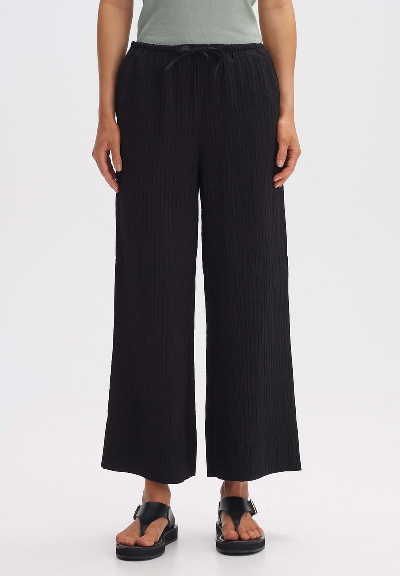 Black wide-leg pants with a textured, ribbed design, featuring an elastic waistband and adjustable drawstring. Flat front pockets are visible.