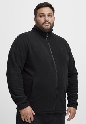 Chaqueta de forro polar negra con cremallera y cuello alto, bolsillos frontales y una textura suave. Diseño minimalista con un pequeño logo en el pecho.
