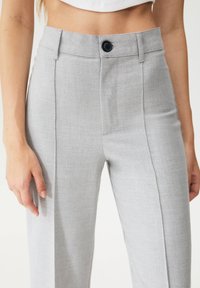 Lichtgrijze op maat gemaakte broeken van zacht materiaal. Bevat een voorkreuk, een enkele knoopsluiting en zijzakken.