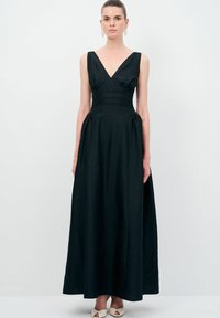 Sort maxikjole med V-hals, tætsiddende overdel, struktureret stof og plisserede detaljer. Foret med brede stropper og en flydende silhuet.
