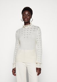 Pullover di colore crema chiaro in tessuto a maglia texture, con scollatura arricciata e maniche lunghe e aderenti. Materiale morbido e leggero.