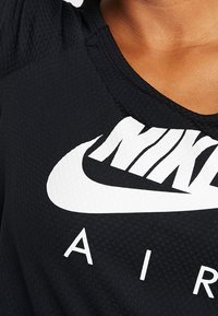 Top atlético negro con un tejido texturizado. Presenta un prominente logo de Nike en blanco y la palabra "AIR" impresa debajo, con cuello redondo.
