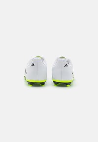 Botas de fútbol blancas con un upper texturizado, acentos verdes en el talón y la suela, y tacos negros para tracción. Tres rayas negras en el costado.