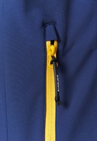 Le tissu d'extérieur bleu marine présente une fermeture éclair jaune avec une languette de tirage. La fermeture éclair est placée dans une poche latérale, mettant en valeur des couleurs contrastantes.