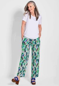 Witte top met korte mouwen gecombineerd met wijde, gebloemde broek in groene, blauwe en zwarte tinten. Houten blokhakken met blauwe banden.