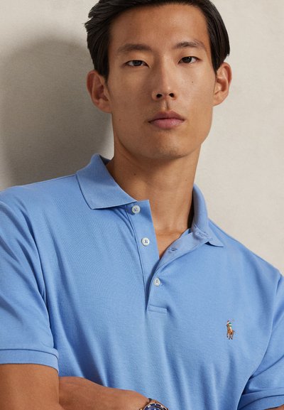 Polo azul claro em algodão, com colarinho clássico, abertura com dois botões e pequeno logótipo bordado no peito.