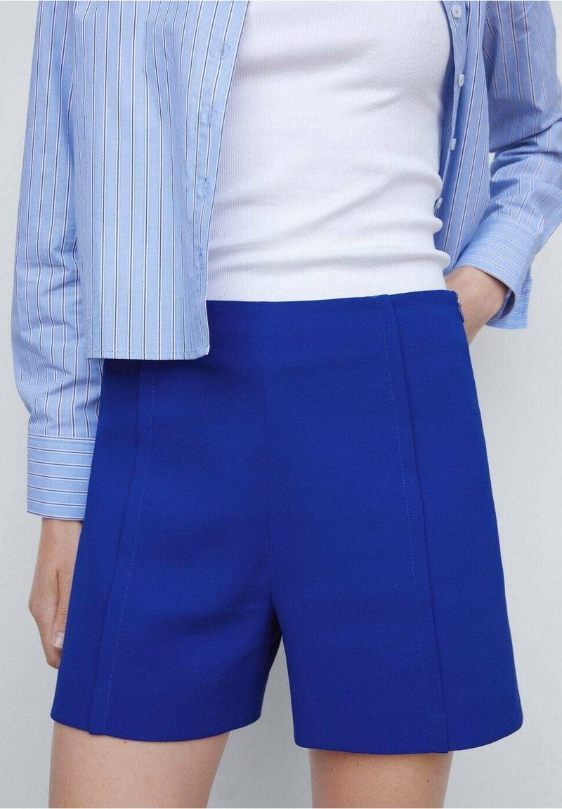 Pantalones cortos azules a medida con una textura suave, que presentan una cintura alta, paneles laterales y líneas limpias, combinados con una camisa a rayas azul clara.