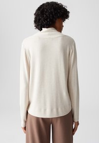 Crèmewitte blouse met lange mouwen, een zachte textuur, een ronde halslijn en een ontspannen pasvorm, gecombineerd met een bruine broek. Simpel en minimalistisch ontwerp.