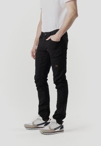 Pantalones cargo negros de corte slim, con múltiples bolsillos y un detalle sutil de parche. Combinados con zapatillas grises y blancas.