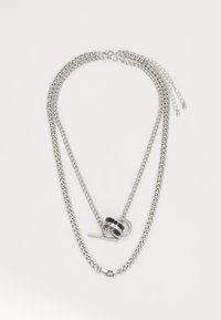 Collier en chaîne multi-couches argenté avec des maillons de tailles variées, mettant en avant un pendentif noir et argenté ainsi qu'un détail de fermoir à bascule.