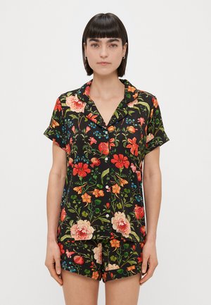 Ensemble de pyjama à manches courtes en tissu noir, orné de fleurs rouges, orange et bleues vives, comprenant une chemise à boutons et un short assorti.