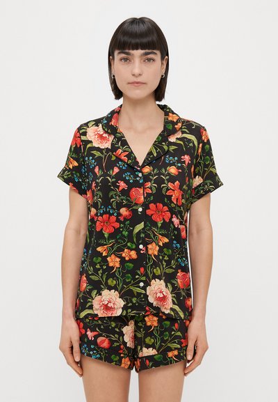 Completo pigiama a maniche corte in tessuto nero, con vivaci fiori rossi, arancioni e blu, composto da una camicia con bottoni e pantaloni corti coordinati.