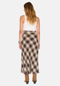 Jupe maxi à carreaux brun, crème et beige avec un design évasé, associée à des bottes à cheville beige. Dotée d'une taille ajustée et d'un tissu fluide.