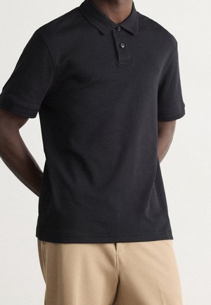 Schwarzes Poloshirt mit kurzen Ärmeln, schlanker Schnitt, Kragen, dreiknöpfige Knopfleiste, dezentes Logo auf der Brust, aus glattem Baumwollstoff hergestellt.