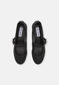Black flat shoes with a round toe, featuring a glossy finish, an adjustable strap, and a decorative silver buckle accent.