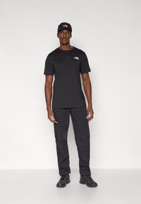 Μαύρο κοντομάνικο μπλουζάκι και παντελόνι με το λογότυπο The North Face. Το σύνολο συνδυάζεται με μαύρα αθλητικά παπούτσια και καπέλο στο ίδιο χρώμα. Απλός σχεδιασμός.