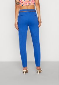 Modré úzké kalhoty s hladkou texturou, se sofistikovaným střihem a zadními kapsami. Nosené s květinovým topem a podpatky.