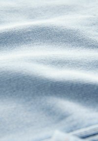Tessuto azzurro chiaro con una superficie liscia e leggermente strutturata. Il materiale appare morbido e flessibile, con trame sottili e delicate.