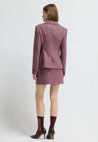 Skræddersyet blazer og mini nederdel sæt i struktureret mørk pink stof, med klassisk krave, strukturerede skuldre og dekorative knapper.