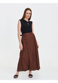 Czarny bezrękawnik z detalem w kształcie dziurki, połączony z długą, brązową spódnicą o kroju wrap z wiązaniem w talii oraz gładką, zwiewną teksturą.