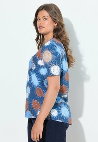 Camisa de algodón azul de manga corta con patrones circulares abstractos y coloridos en naranja, blanco y azul claro. Abertura lateral en el dobladillo.