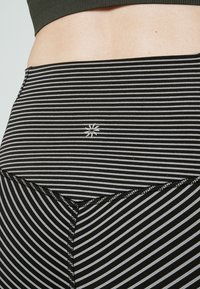 Leggings de sport à rayures noires et blanches avec une taille élastique, des coutures plates et un petit logo sur le devant en bas.