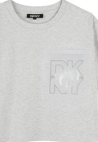 Camiseta de algodón gris con cuello redondo, mangas cortas y un bolsillo en el pecho. El bolsillo tiene una superposición transparente con un diseño de corazón.