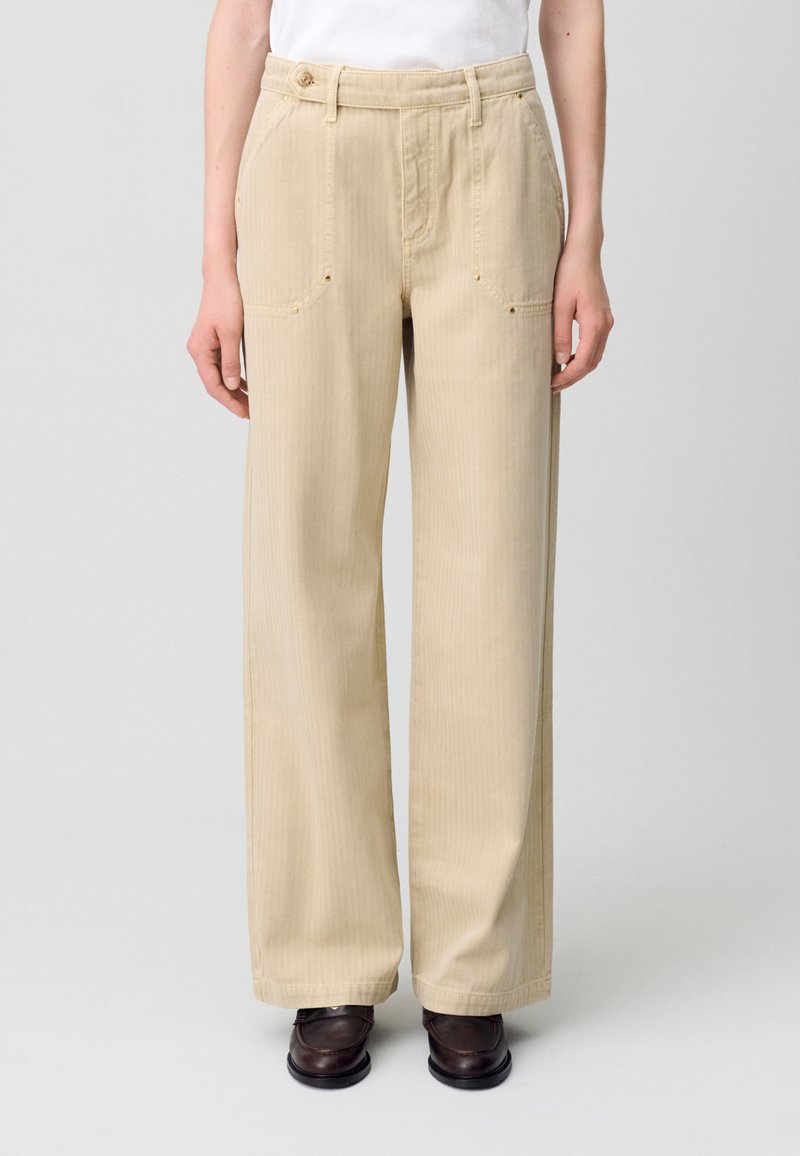 Pantalones de pierna ancha beige, fabricados en tejido texturizado, que cuentan con bolsillos frontales, cierre con botón y detalles de costura sutiles.