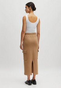 Jupe midi beige avec une taille à cordon, poches latérales, fente au dos et une texture lisse et douce. Accompagnée d'un débardeur blanc ajusté.