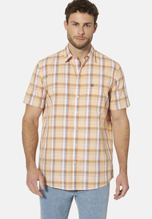 Mann trägt kurzärmeliges orange-weiß kariertes Hemd mit Knöpfen und hellblaue Jeans, steht vor einfachem Hintergrund.