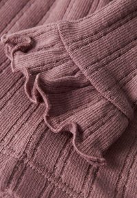 Maglione a coste in morbido malva, con orlo arricciato. La trama presenta linee in rilievo, aggiungendo profondità al tessuto.