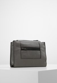Bolso de cuero gris con forma rectangular, un bolsillo frontal con cremallera y costuras en contraste. Textura suave y diseño minimalista.