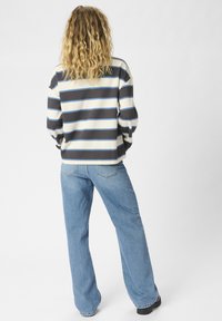 Chemise à rayures à manches longues en bleu marine, crème et bleu clair ; associée à un jean large bleu clair. Matériau en coton, coupe décontractée.