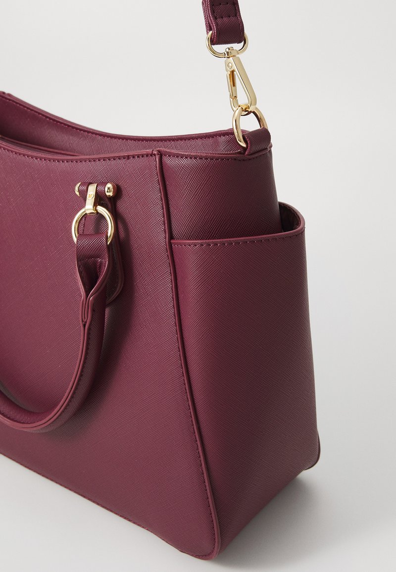 Bolso de mano de imitación cuero burdeos con una forma estructurada, textura suave, acentos de hardware dorado y un bolsillo lateral para almacenamiento adicional.