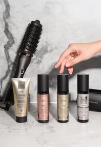 Ręka sięga po jedną z trzech butelek ghd rehab do pielęgnacji włosów na marmurowej powierzchni obok okrągłej szczotki i tubki z produktem do włosów.