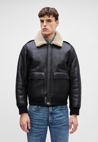 Black leather bomber jacket with a cream shearling collar, two front pockets, ribbed cuffs, and a fitted silhouette.
