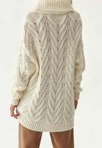 Sweter pleciony w kolorze kremowym z masywnym kołnierzem, w luźnym fasonie i skomplikowanym, fakturowanym wzorem. Ribbowane mankiety i dół.