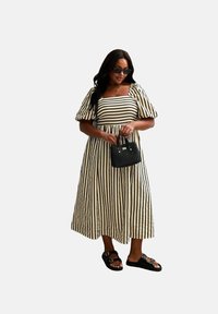 Gestreiftes Maxikleid in Creme und Schwarz mit Puff�ärmeln, quadratischem Ausschnitt und tailliertem Bund. Schwarze Handtasche und flache Sandalen mit Schnallen.