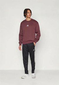 Bordový mikina s bielym logom, kombinovaná s čiernymi teplákmi s bielymi pruhmi a bielymi športovými topánkami.