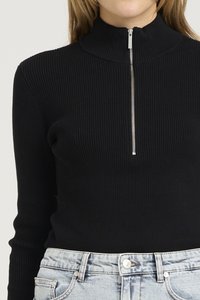 Maglione a collo alto nero a coste con mezzo zip, abbinato a jeans a vita alta in denim chiaro. Materiale testurizzato in tutto.