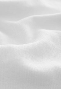 Tissu blanc doux avec des plis lisses et subtils et un motif de texture gaufrée fine sur toute la surface.