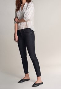 Vit, texturerad blus med vertikala ränder; mörkblå smala jeans; svarta spetsiga slip-on skor. Enkelt design, avslappnad outfit.