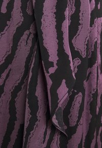 Tela negra y púrpura con un diseño abstracto ondulado. El material parece suave y texturizado, con formas irregulares y acentos.