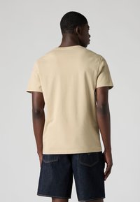 Beige cotton t-shirt with a crew neck and short sleeves, worn with dark denim shorts, showing a minimalistic design and a relaxed fit.