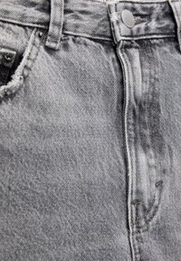 Šedé džíny z denimu s vysokým pasem, přišitým předním kapsou a stříbrným knoflíkem. Tkanina má mírně opotřebovaný vzhled s jemnými záhyby.