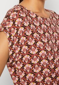 Rose-colored blouse with a floral and shell pattern, featuring short sleeves and a round neckline, made from lightweight, textured fabric.